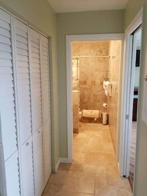 Un couloir menant à une salle de bain équipée d’une douche, de toilettes et d’un porte-serviettes.