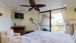 A bedroom with a bed, a ceiling fan, a TV, a balcony with a view, and a window with curtains.