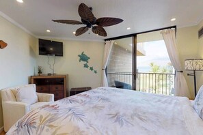 A bedroom with a bed, a ceiling fan, a TV, a dresser, and a balcony with a view.