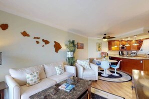 A living room with a sofa, chairs, a coffee table, and a kitchen area with wooden cabinets and a dining table.