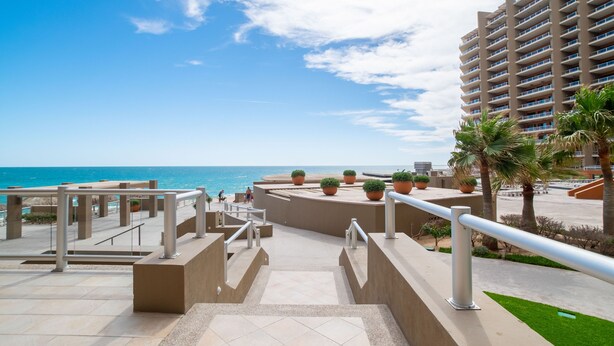 Ein modernes Hotel mit Meerblick, das einen zentralen Innenhof mit Kübelpflanzen und eine Treppe zum Strand bietet.