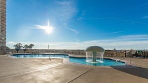 A rooftop pool with a water fountain, surrounded by a fence and palm trees.