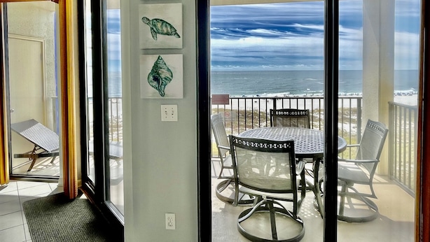 A balcony with a table and chairs, a view of the ocean, and three shell artworks on the wall.
