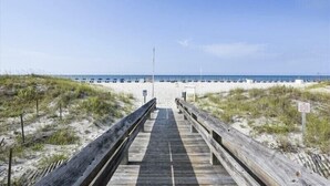 A wooden boardwalk leading to a beach with sand dunes and a clear sky.