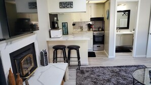 Une cuisine moderne dotée d’un îlot central, de deux tabourets de bar, d’une cheminée et d’un coin repas avec un comptoir en marbre.