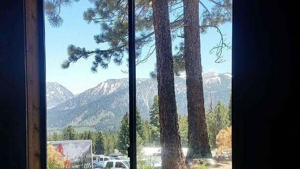 Une fenêtre donnant sur une vue de grands pins et, au loin, sur des montagnes.