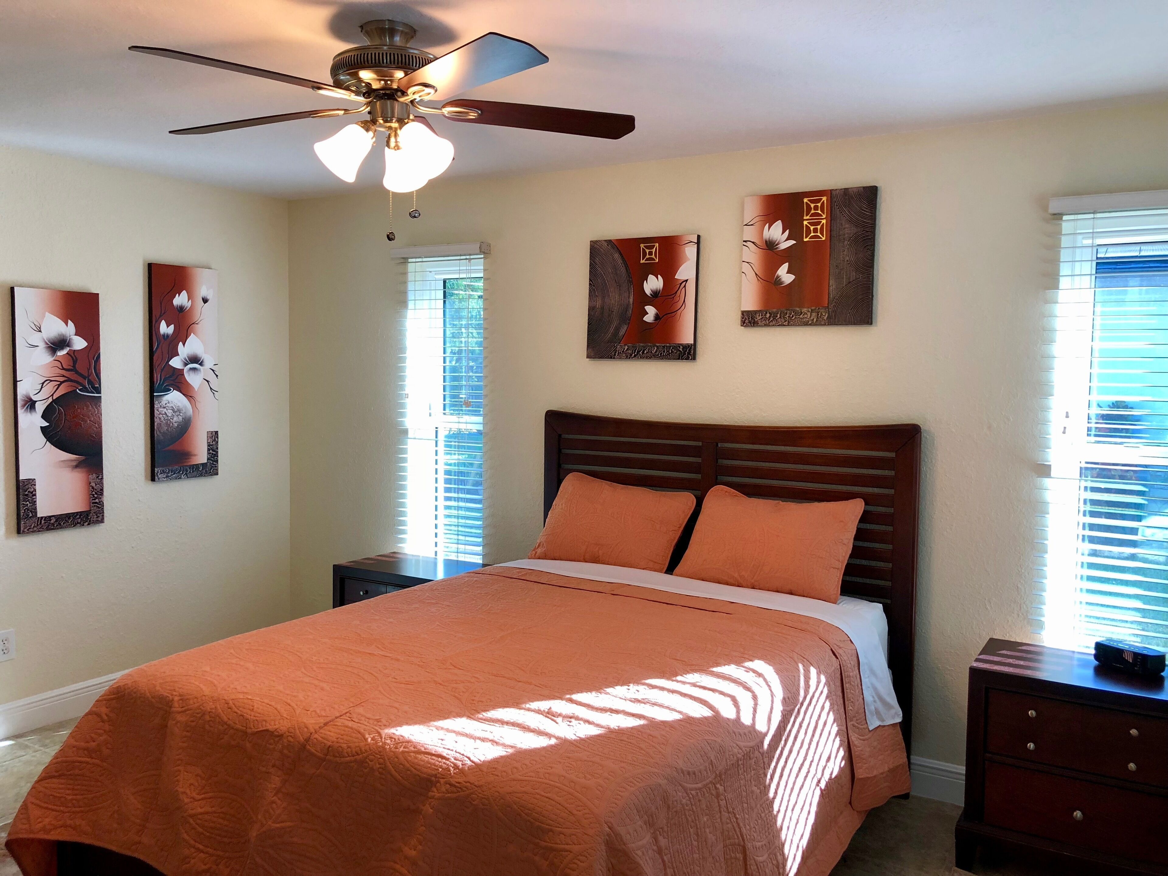 A bedroom with a bed, a ceiling fan, and artwork on the walls.
