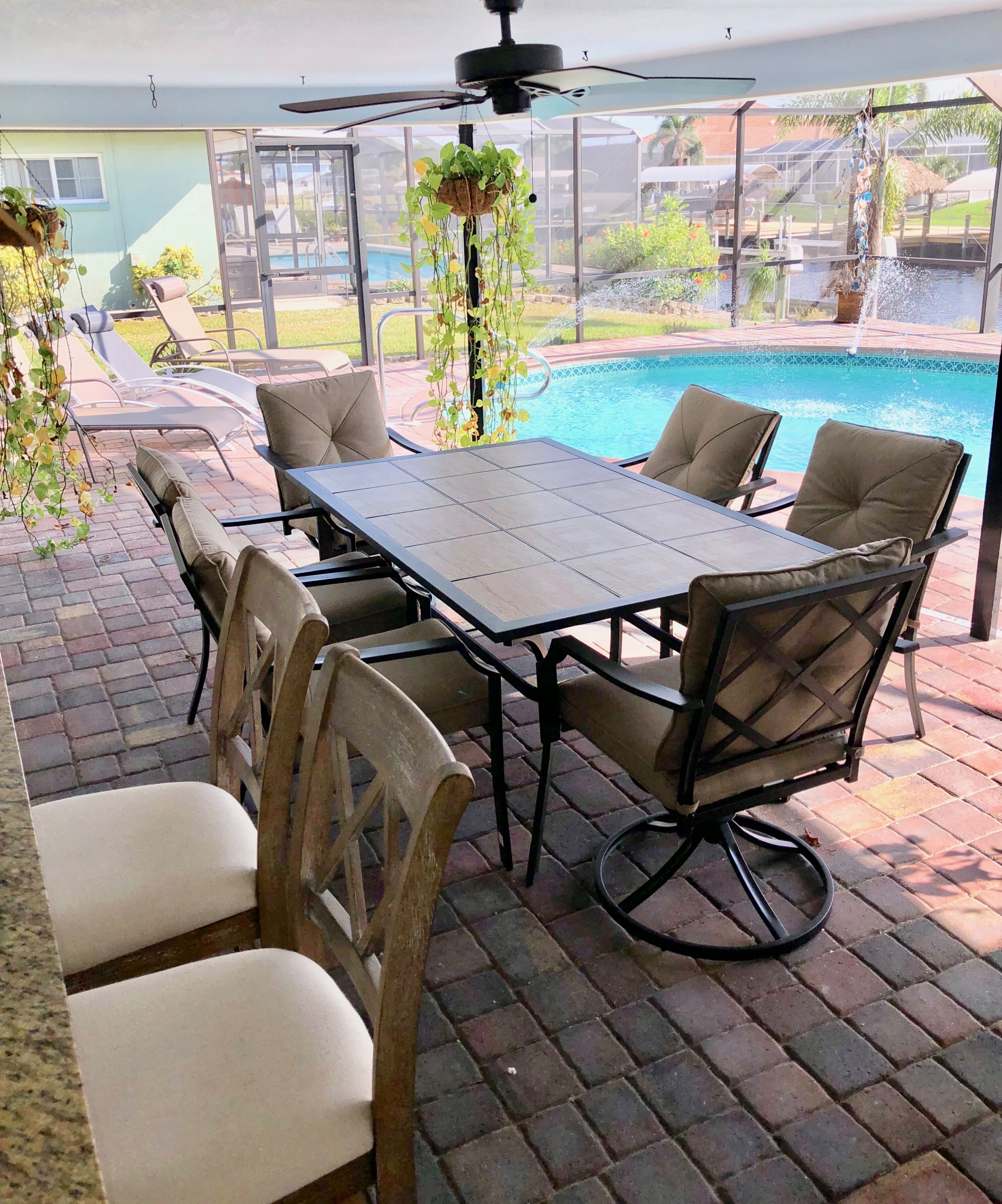 Un patio exterior con mesa y sillas, un ventilador de techo y vistas a una piscina.