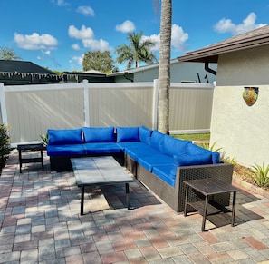 Relax on the patio with a comfortable sofa, a metal table, and a wicker chair.