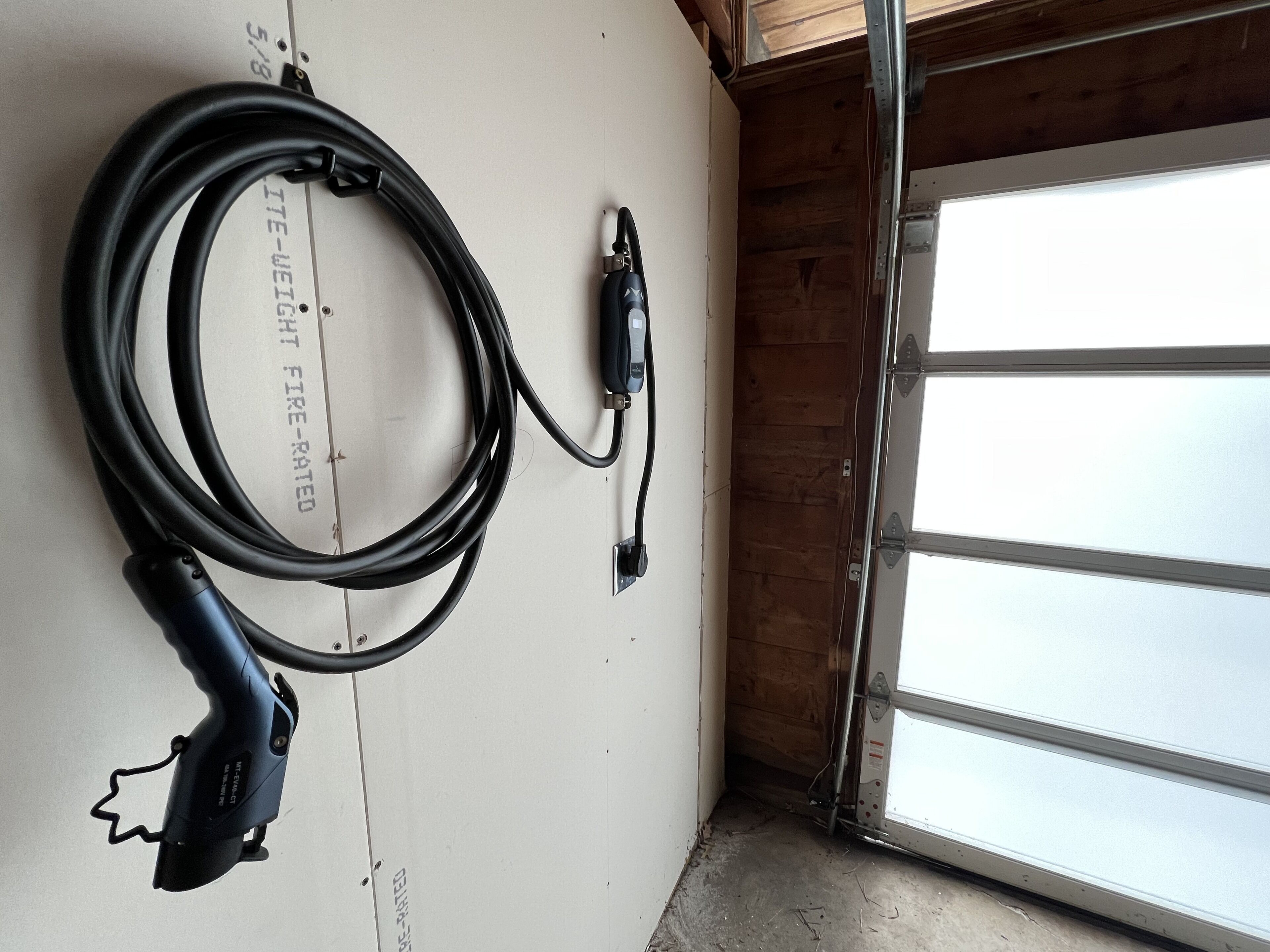 Eine Garage mit weißer Wand, schwarzem Verlängerungskabel und einer Garagentür.