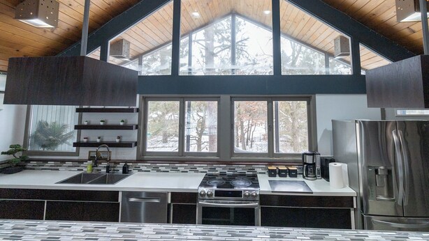 A modern kitchen with a large island, built-in appliances, and a view of trees through large windows. - Waterfront Home with Pontoon, Movie & Game Room-Perfect for Families & Getaways! (Park Rapids)