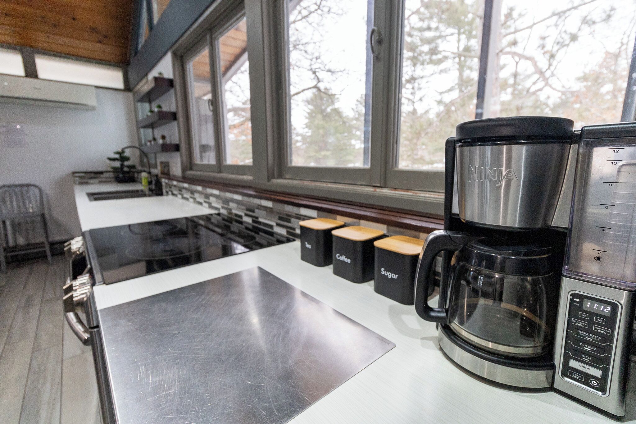 Una cucina moderna con una macchina da caffè, un fornello e una finestra vista alberi.