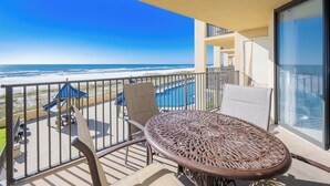 Un balcon avec vue sur l’océan, une piscine et un espace repas avec des chaises et une table.
