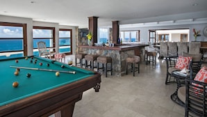 Une table de billard avec des billes, un bar avec des tabourets et un espace salon avec des chaises.
