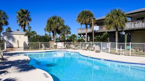 A swimming pool with a white fence, palm trees, and a building with a balcony. - Large Garage for Boat, Shared Pool , Pet Friendly, Golf Cart Access (Port Aransas)