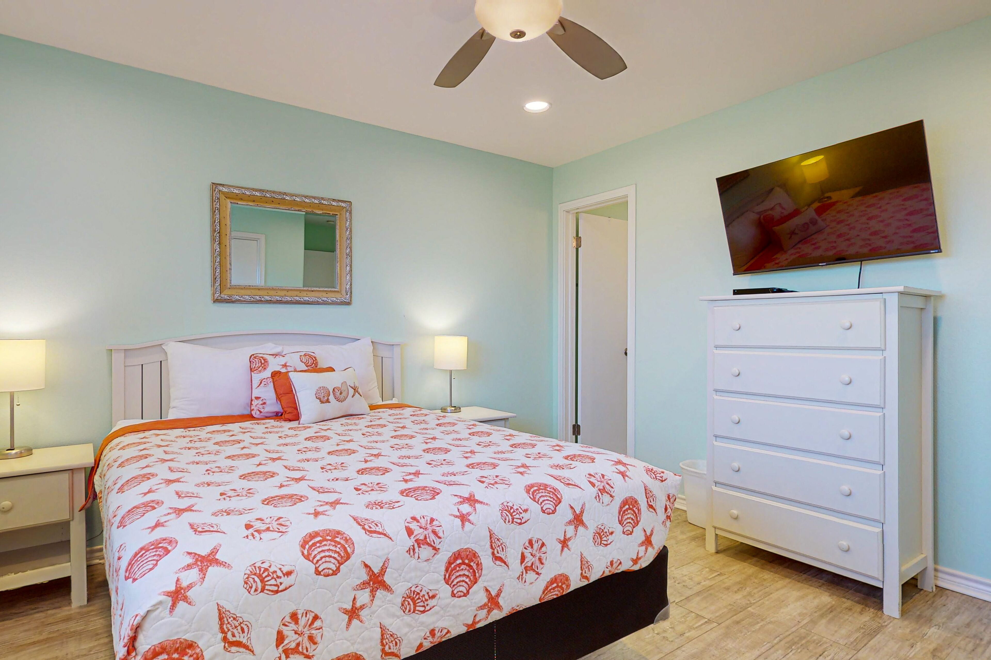 A bedroom with a bed, nightstands, a dresser, a ceiling fan, a TV, and a mirror.