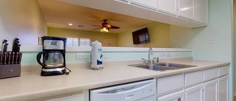 A kitchen with white cabinets, a coffee maker, a dishwasher, and a ceiling fan.