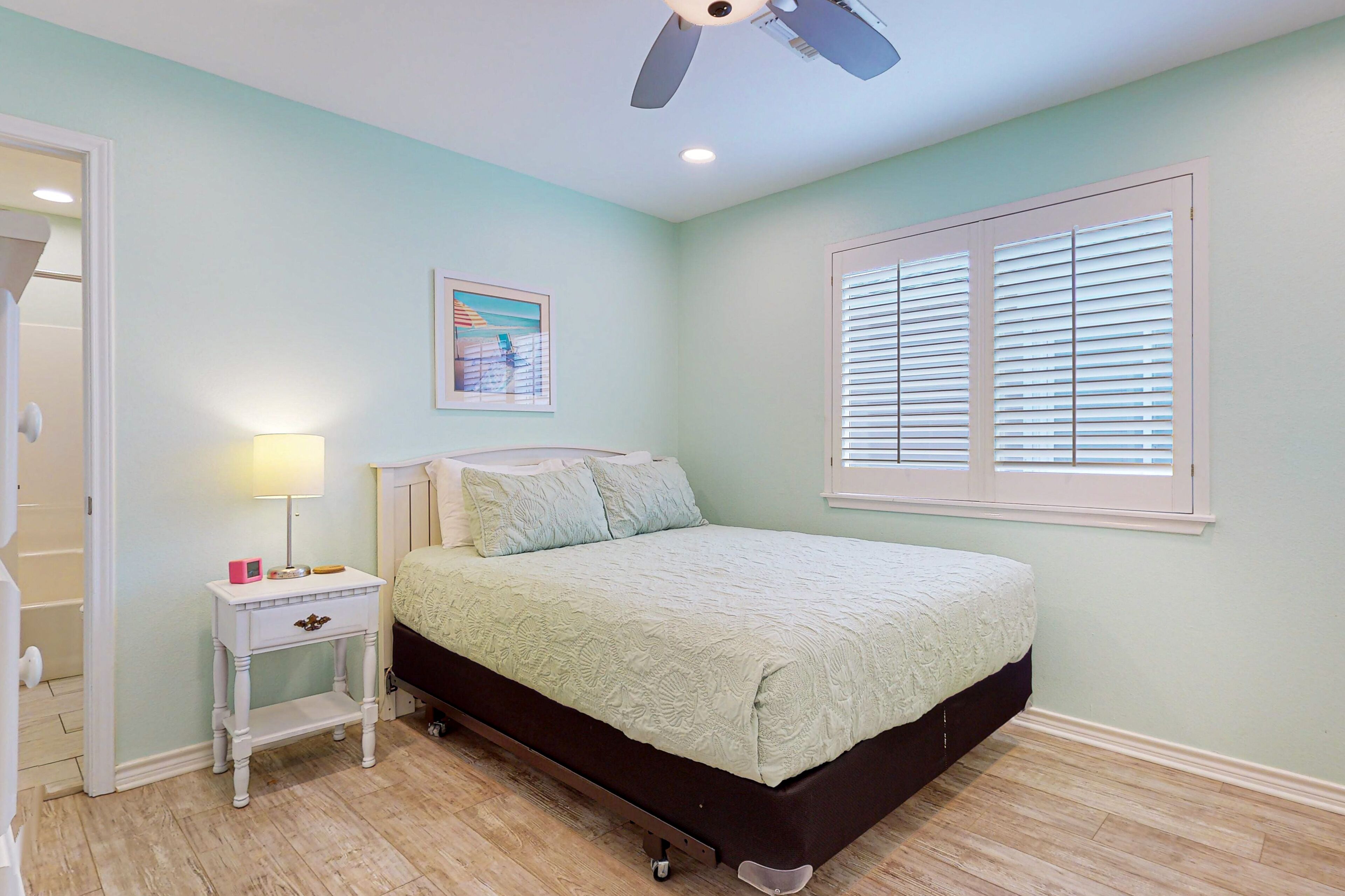 A bedroom with a bed, a nightstand, a ceiling fan, a window with blinds, and a door.