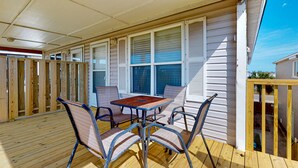 A covered patio with a wooden deck, metal table, and cushioned chairs. - Large Garage for Boat, Shared Pool , Pet Friendly, Golf Cart Access (Port Aransas)