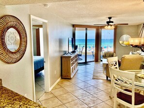 A hotel room with a balcony, a TV, a dining area, and a view of the beach.