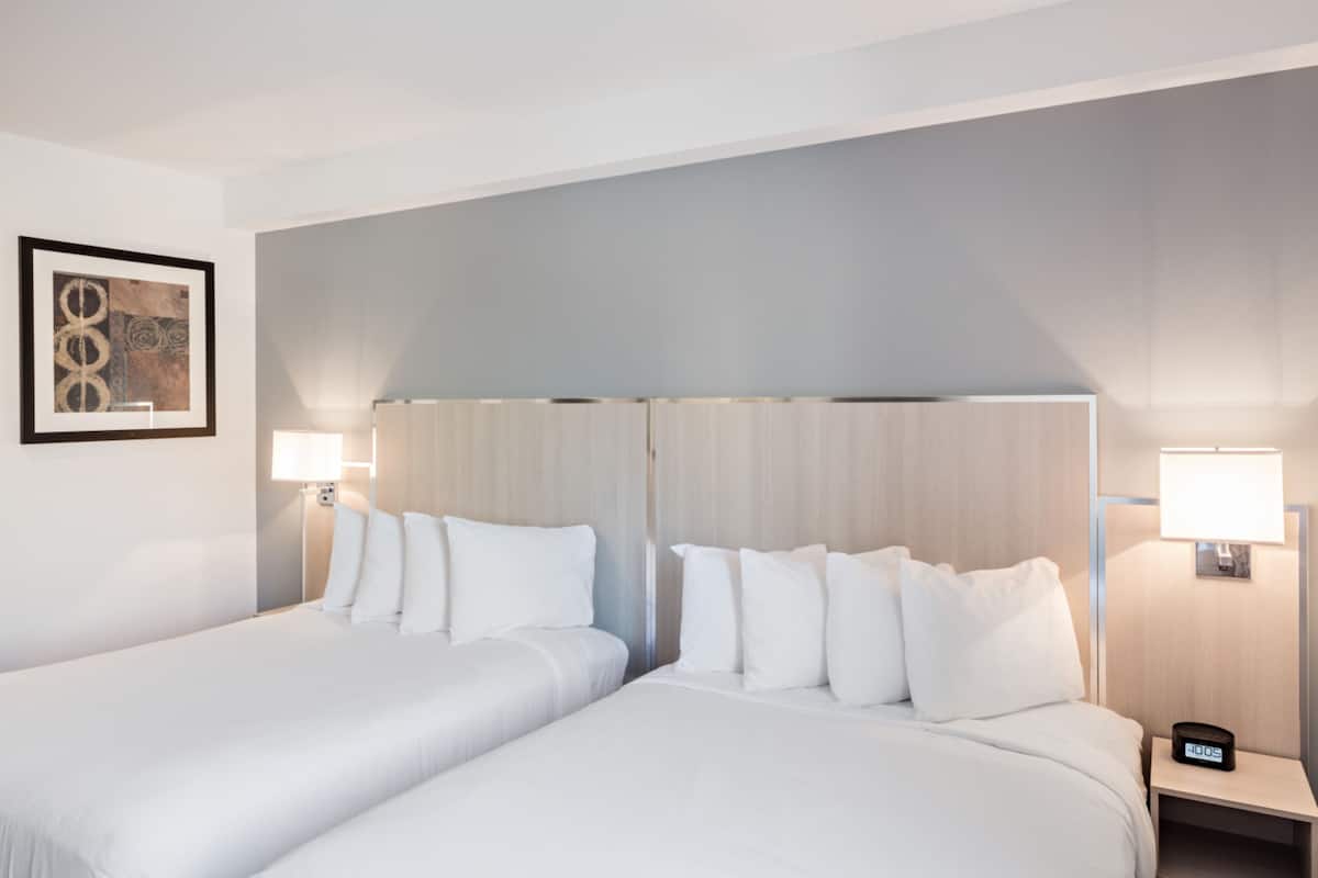 Habitación de hotel con dos camas, una obra de arte enmarcada en la pared y lámparas de noche.