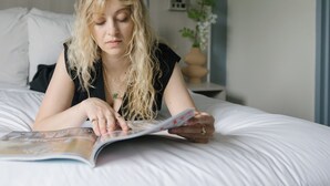 A person lying on a bed in a room with a headboard, a bedside table with a lamp, and a wall-mounted air conditioning unit. - The Gatsby Hotel (New York)