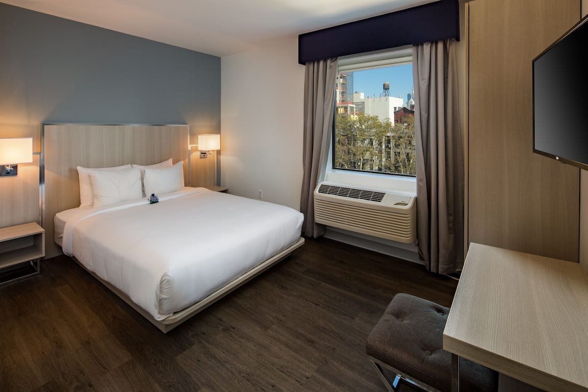 Habitación de hotel con una cama grande, lámparas de noche, una ventana con cortinas, un equipo de aire acondicionado y un televisor de pantalla plana.
