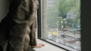 A person leaning on a window sill with a view of a cityscape and buildings. - The Gatsby Hotel (New York)