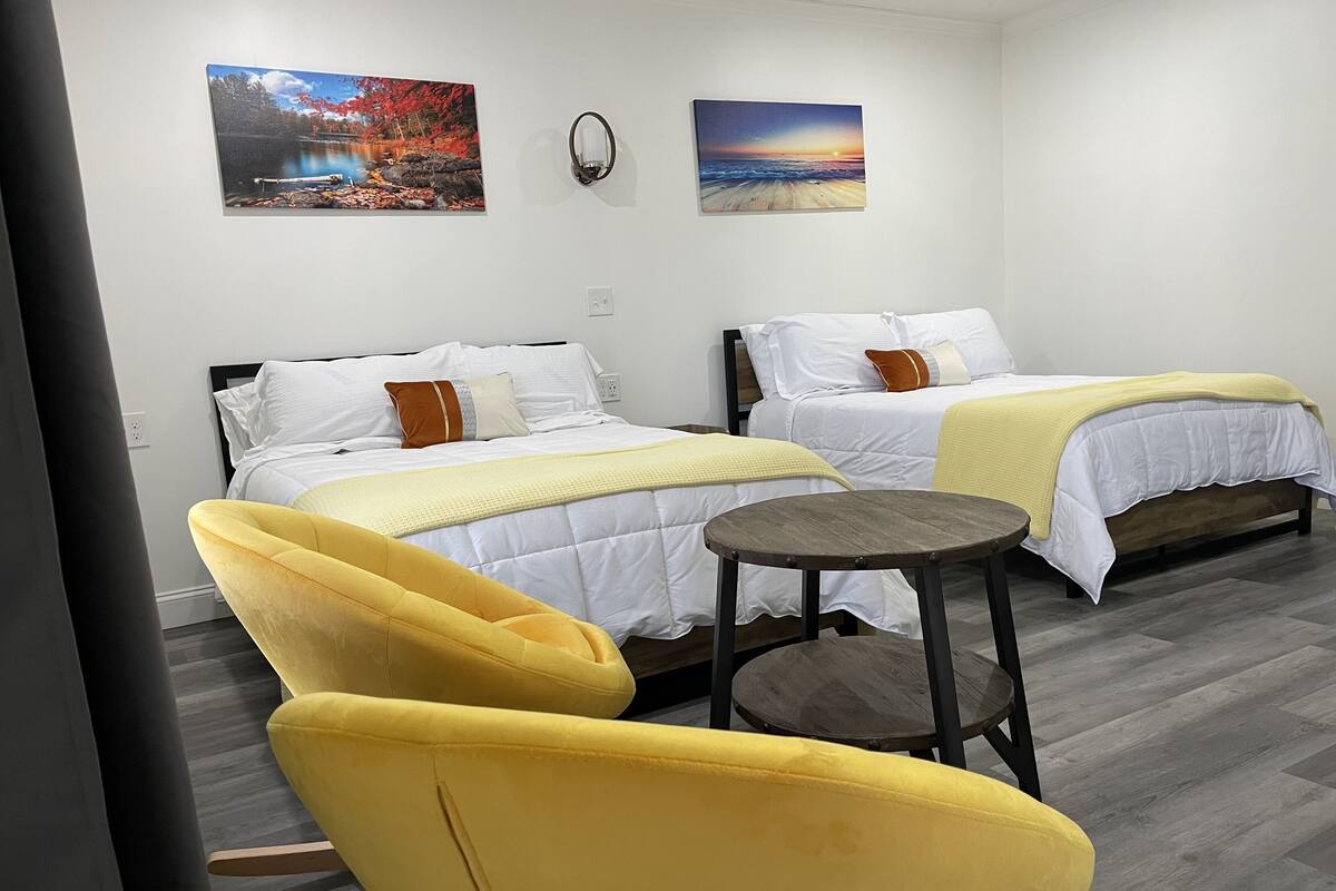 A hotel room with two beds, a small round table, and a yellow armchair.