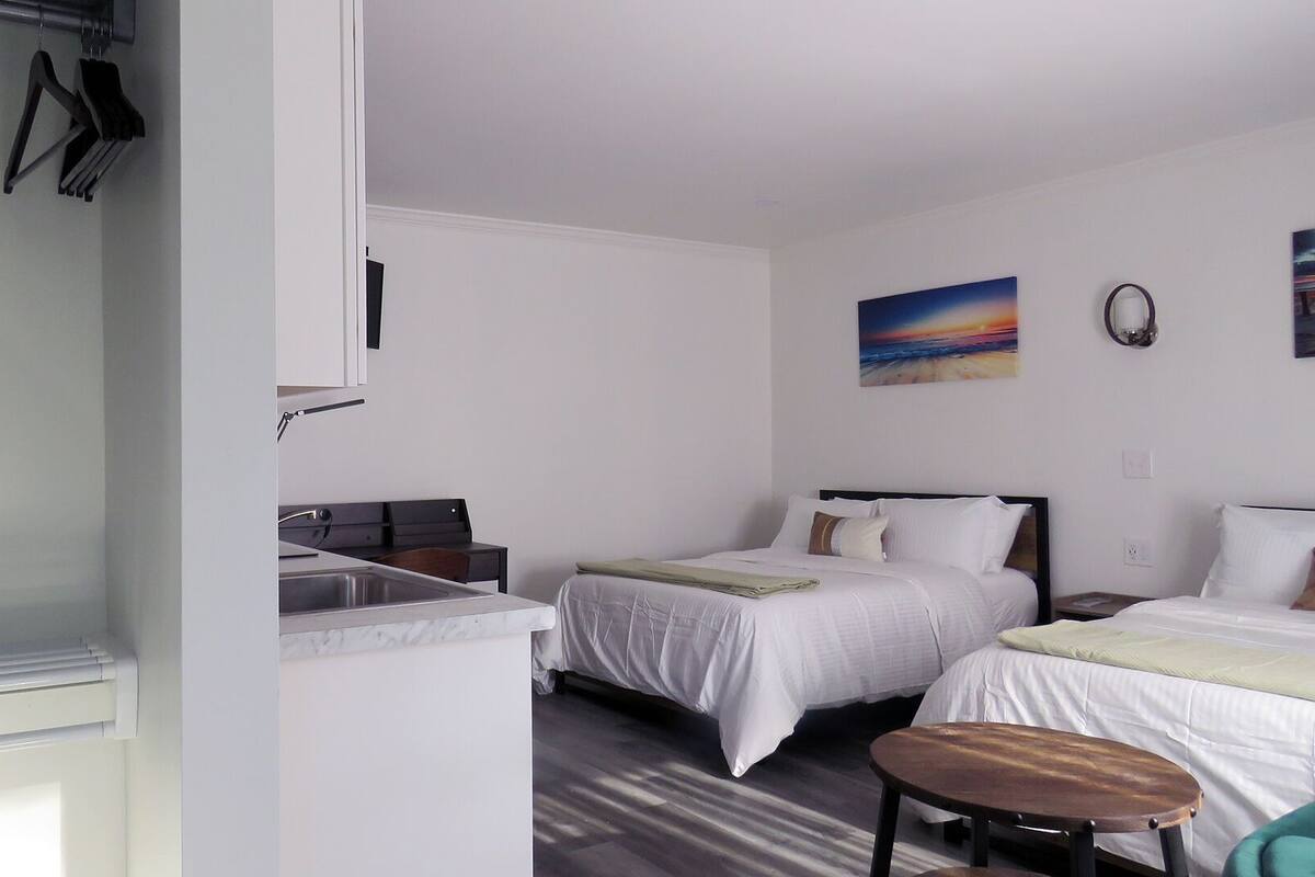 A hotel room with two beds, a small table, a desk, and a painting on the wall.