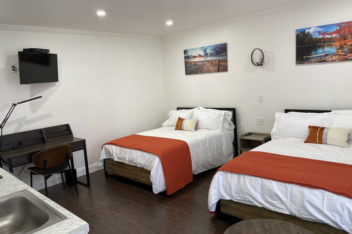 A hotel room with two beds, a desk, a chair, a TV mounted on the wall, and artwork on the walls.