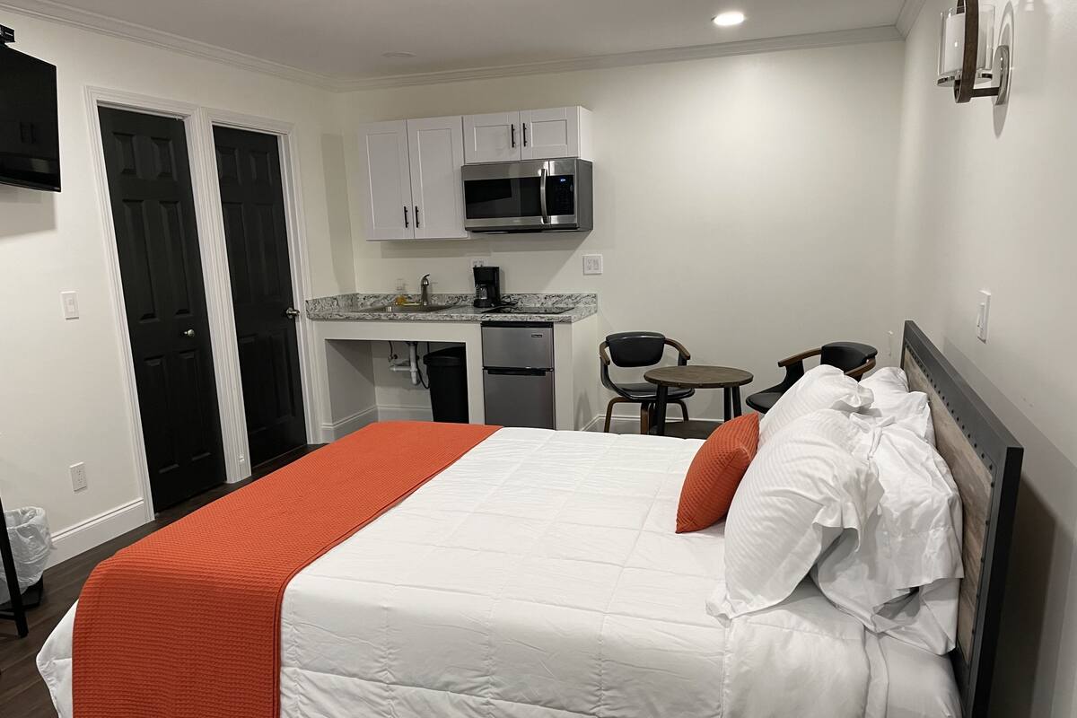 A hotel room with a bed, a small kitchenette, a microwave, and a seating area with chairs.