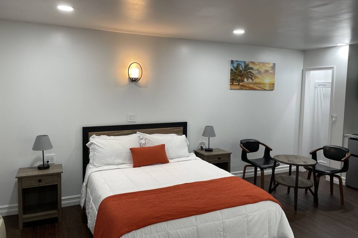 A hotel room with a bed, bedside tables, a lamp, a chair, and a painting on the wall.