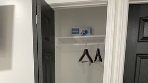 Un pasillo con una puerta negra a la izquierda, una puerta blanca a la derecha y una pared blanca con un estante sobre las puertas.