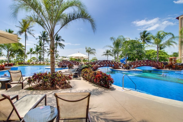 A pool area with lounge chairs, a bridge, and palm trees.