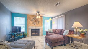 A living room with a fireplace, a television, and a ceiling fan.