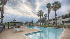 A swimming pool with lounge chairs, palm trees, and a covered seating area.