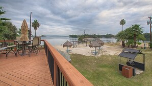 A wooden deck with outdoor furniture, a grill, and umbrellas overlooking a body of water.