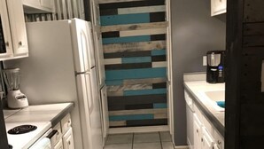 A narrow kitchen with white cabinets, a refrigerator, a coffee maker, and a striped backsplash.