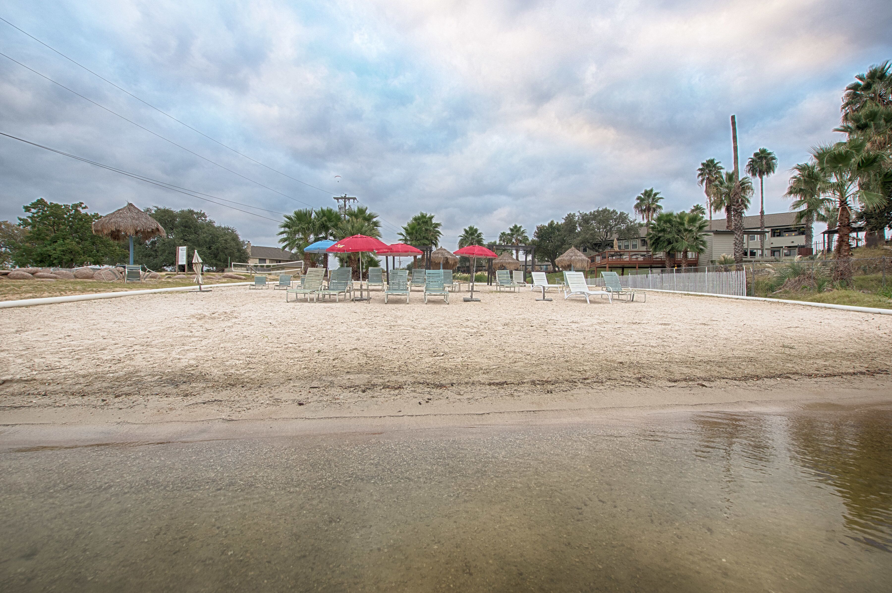 A beachside area with several umbrellas and lounge chairs, a thatched-roof structure, and palm trees.