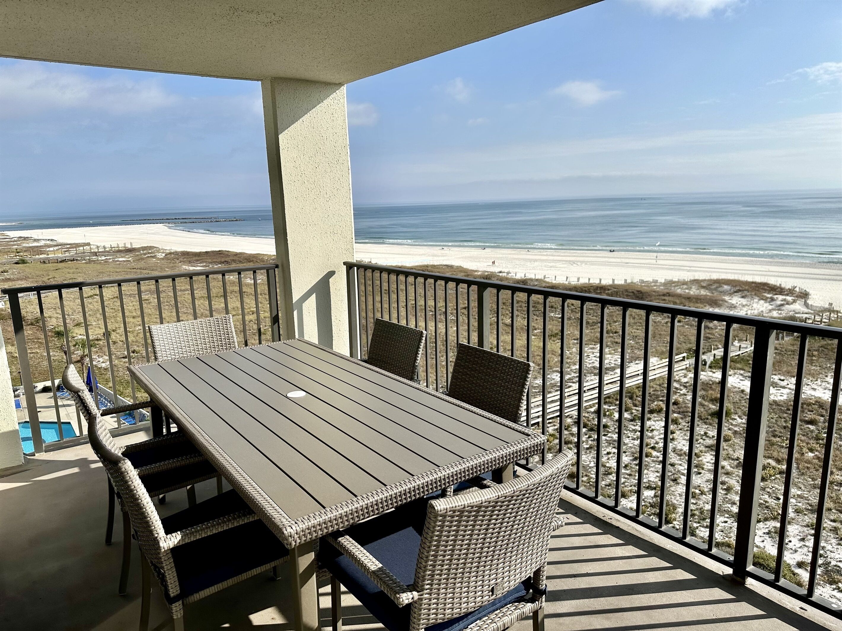 A balcony with a table and chairs, overlooking a beach and ocean.