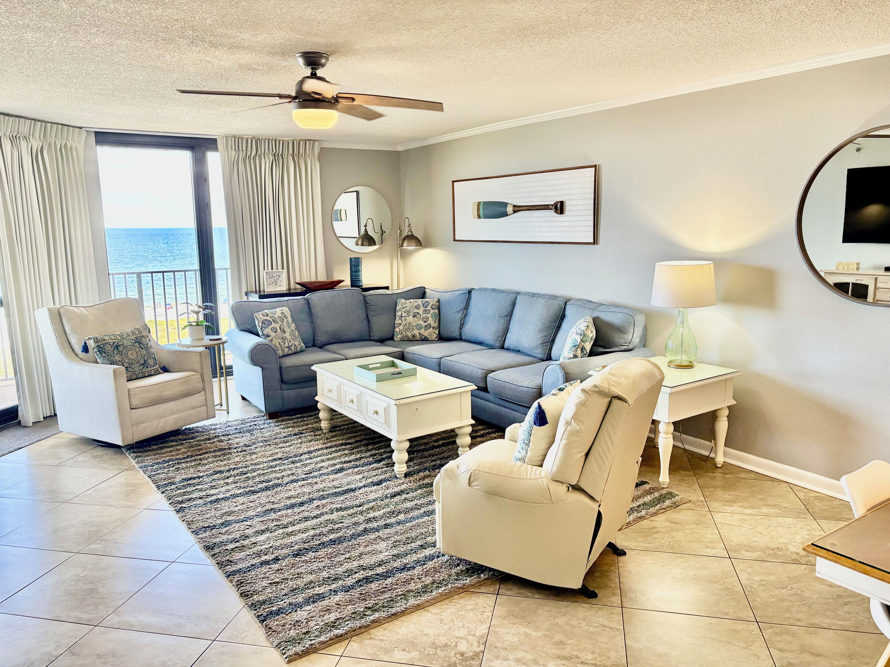 A living room with a sofa, armchairs, a coffee table, and a ceiling fan.