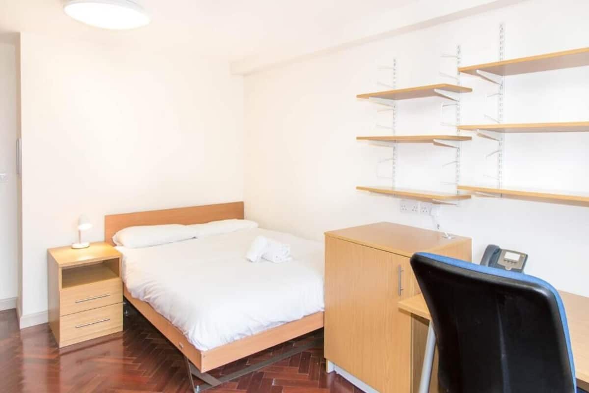Un dormitorio con cama, mesita de noche, escritorio, silla y estanterías.