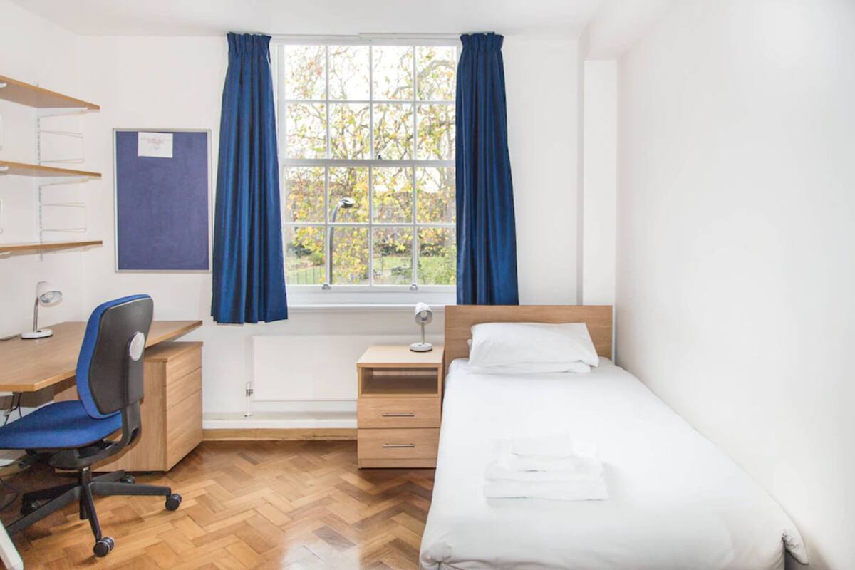Un dormitorio con escritorio de madera, silla y cama con ropa de cama blanca.