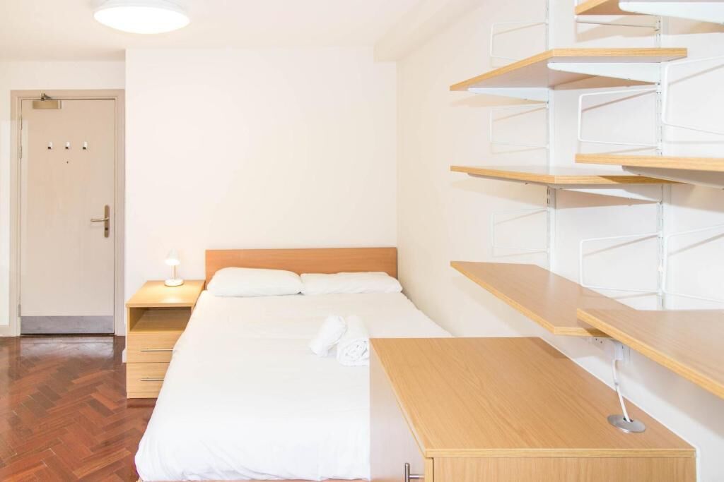 A hotel room with a bed, a bedside table, a lamp, and built-in shelves.