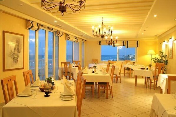 A dining area with tables set for a meal, large windows with a view, and a chandelier. - Hotel Flamingo Beach (Mezraia)