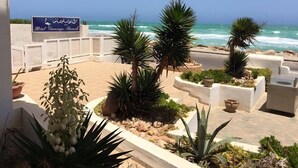 Une terrasse d’hôtel avec vue sur l’océan, agrémentée de plantes en pot et d’une enseigne indiquant « Hôtel Flamingo Beach ».