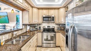 Une cuisine moderne dotée d’appareils électroménagers en acier inoxydable, de plans de travail en granit et d’armoires de couleur beige.