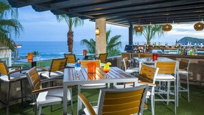 Ein Außenbereich mit Tischen, Stühlen und einer Bar voll mit Flaschen, mit Blick auf das Meer.