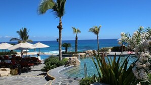Ein Poolbereich eines Resorts mit Palmen, Liegestühlen und Blick auf den Ozean.